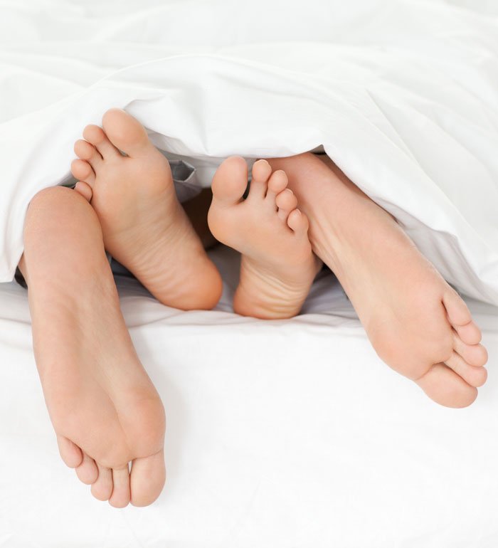 Close up of male and female feet sticking out from bed cover