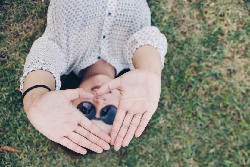 woman lying on grass holding hands in the air